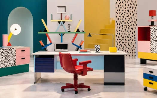 Arredi per ufficio ispirati a Memphis Milano, con scrivania, sedia rossa, libreria geometrica e mobili colorati.